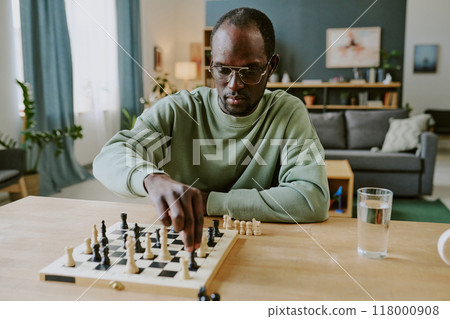 Young African American man solving chess problem while spending spare time in living room at home 118000908
