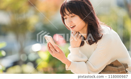 Smiling woman looking at her smartphone outdoors in autumn Smiling woman looking at her smartphone outdoors in autumn 118000987