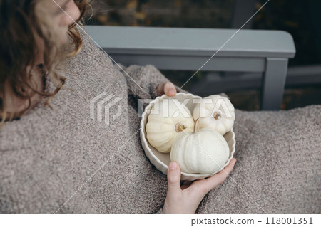 Young girl, woman wearing brown wool sweater holding bowl of little white pumpkins for autumn decorations. Fall festive still life. Halloween, Thanksgiving holiday. Cozy lifestyle. Blurred background 118001351
