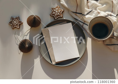Christmas still life. Blank greeting card, invitation mockup on ceramic plate in sunlight. Star gingerbread cookies, Paper Christmas ornaments balls. Cup of coffee. Checkered plaid. Winter scene Christmas still life. Blank greeting card, invitation mockup on ceramic plate in sunlight. Star gingerbread cookies, Paper Christmas ornaments balls. Cup of coffee. Checkered plaid. Winter scene 118001360