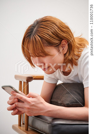 A woman relaxing at home using a smartphone 118001736