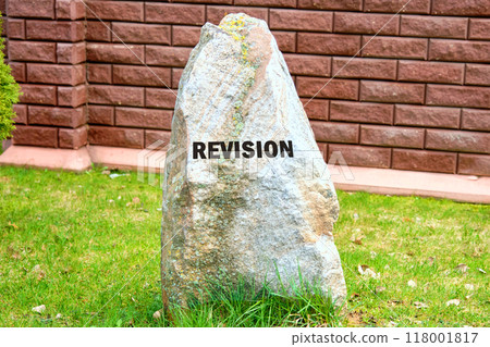 REVISION written on a stone on the background of a fence, red brick walls 118001817