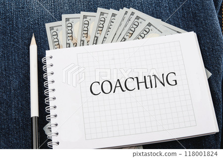 COACHING written on a checkered notebook against the background of American paper bills COACHING written on a checkered notebook against the background of American paper bills 118001824