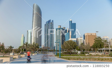 Corniche boulevard beach park along the coastline in Abu Dhabi timelapse with skyscrapers on background. 118003250