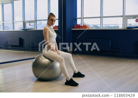 Young woman in activewear exercises on stability ball in gym setting 118003429