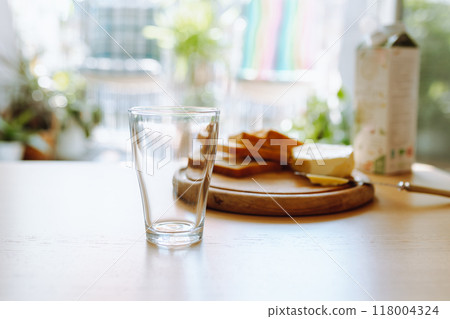 An empty glass stands on table, in background there is bread, butter, milk. Breakfast An empty glass stands on table, in background there is bread, butter, milk. Breakfast 118004324