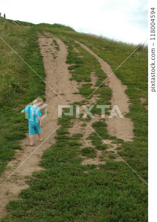A barefoot boy in blue clothes is climbing a mountain along a country road A barefoot boy in blue clothes is climbing a mountain along a country road 118004594