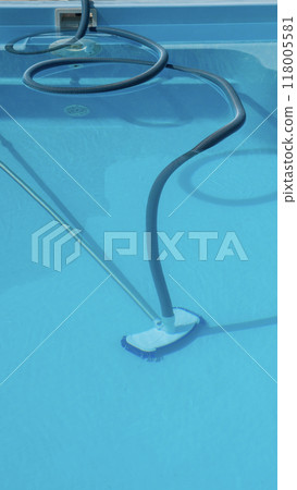 A pool cleaning hose and vacuum head positioned in a nearly empty pool, emphasizing pool upkeep and sanitation. A pool cleaning hose and vacuum head positioned in a nearly empty pool, emphasizing pool upkeep and sanitation. 118005581