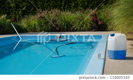 Pool cleaning hose and vacuum head with a large chemical container and water testing kit on the poolside, emphasizing water sanitation and maintenance. Pool cleaning hose and vacuum head with a large chemical container and water testing kit on the poolside, emphasizing water sanitation and maintenance. 118005585