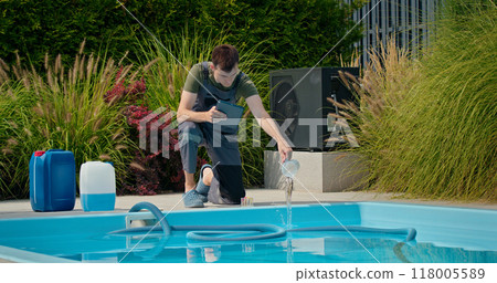 Pool technician pouring liquid into the pool while using a tablet, surrounded by chemical containers and greenery. Pool technician pouring liquid into the pool while using a tablet, surrounded by chemical containers and greenery. 118005589