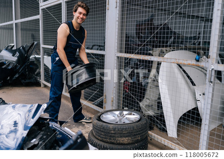 Portrait of friendly mechanic male in uniform changing wheel rim in auto repair workshop. Cheerful repairman working in garage and changing wheel alloy tire. Concept of car service and maintenance. Portrait of friendly mechanic male in uniform changing wheel rim in auto repair workshop. Cheerful repairman working in garage and changing wheel alloy tire. Concept of car service and maintenance. 118005672