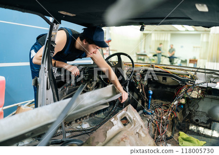Skilled mechanic male inspecting car for useful things for secondary repairs before recycling in automobile repair and renew service station. Concept of professional car repair and maintenance work. Skilled mechanic male inspecting car for useful things for secondary repairs before recycling in automobile repair and renew service station. Concept of professional car repair and maintenance work. 118005730