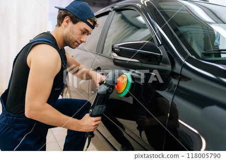 Portrait of skilled mechanic worker polishing door of luxury car in auto repair shop using with orbital polisher. Expert car paint technician using car polisher to polish car with refinement. 118005790