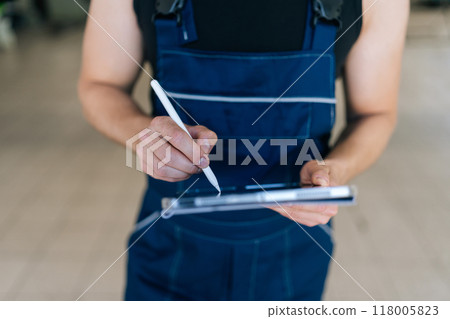 Closeup cropped shot of unrecognizable mechanic male holding digital tablet and using stylus. Close-up of auto mechanic man servicing car, checking engine with diagnostic software on digital tablet. 118005823