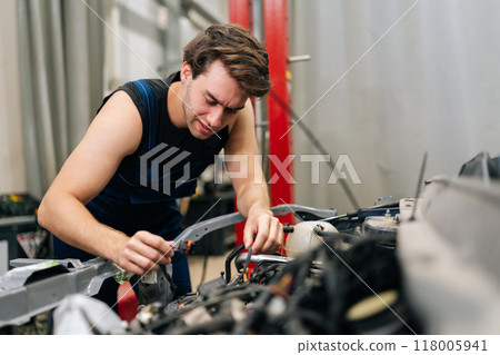Portrait of focused car mechanic male servicing car engine in automobile repair renew service station. Car service repairman examining broken engine. Garage employee conducts vehicle checkup. Portrait of focused car mechanic male servicing car engine in automobile repair renew service station. Car service repairman examining broken engine. Garage employee conducts vehicle checkup. 118005941