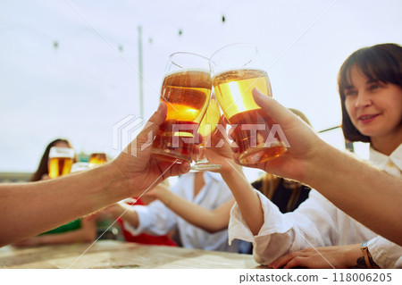 Friends gather around table, raising their glasses in toast to good times. Lively atmosphere and shared laughter make for perfect sunny day. 118006205