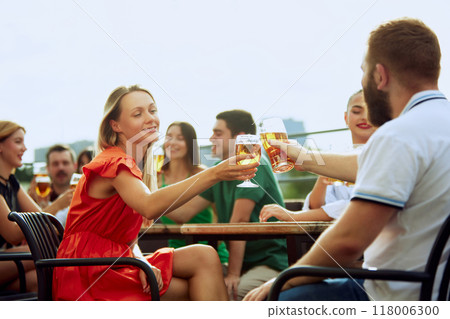 Group of friends sitting at pub terrace talking, drinking alcohol, celebrating meeting after long years. Festive atmosphere. 118006300