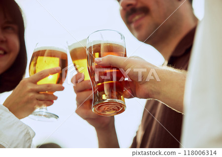 Group of friends clinking beer glasses, celebrating their meeting outdoor. Young people looks happy and cheerful. Concept of Friday mood. Group of friends clinking beer glasses, celebrating their meeting outdoor. Young people looks happy and cheerful. Concept of Friday mood. 118006314
