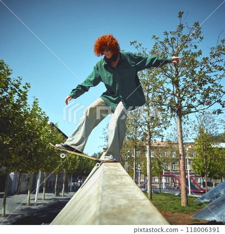 Young stylish guy with red-haired curly hair, in green t-shirt in motion, skater showing tricks and skills while skateboarding in public park. Young stylish guy with red-haired curly hair, in green t-shirt in motion, skater showing tricks and skills while skateboarding in public park. 118006391