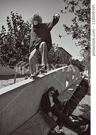 Two riders, active young boys in stylish clothes training outdoors, skateboarding in public park. Black and white photography. 118006395