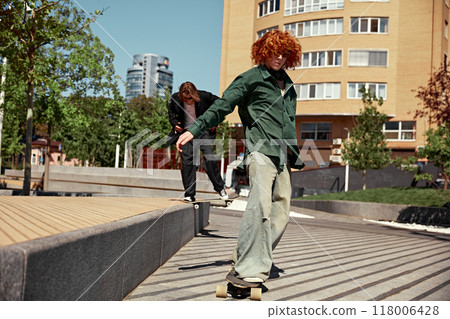 Bringing energy and style. Dynamic image for young boys in stylish outfits in motion in public park, skateboarding with energy 118006428