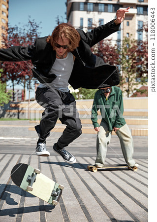 Bringing energy and style. Dynamic image for young boys in stylish outfits in motion in public park, skateboarding with energy Bringing energy and style. Dynamic image for young boys in stylish outfits in motion in public park, skateboarding with energy 118006443