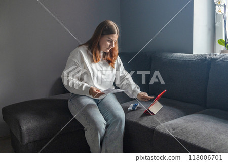 Caucasian woman holds nasal swab and puts into nose for COVID-19 self test at home 118006701