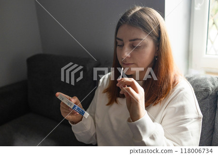 Caucasian woman holds nasal swab and puts into nose for COVID-19 self test at home 118006734