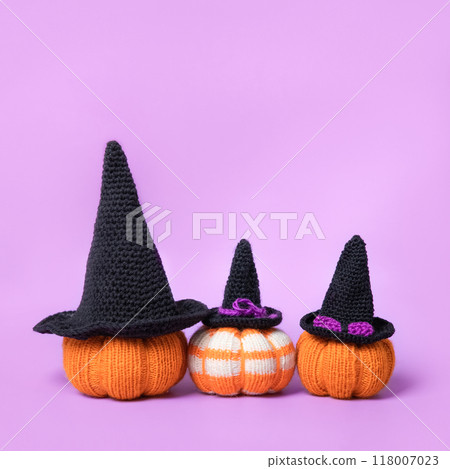 Knitted orange pumpkins with black witch hat on purple background, autumn composition, front view. Halloween concept. 118007023