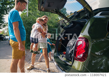 A joyful family of excited children packs their luggage into a spacious car for a thrilling summer road trip 118007421