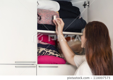 Woman protects knitted items, clothes in a closet from moths. Girl puts moth pill in cupboard, anti-moth for storing woolen and fur clothes, kills moths and other domestic insects. 118007573