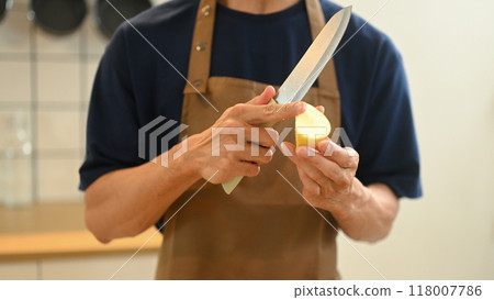 Cropped shot of man peeling an apple with a knife while preparing a healthy dish in a kitchen 118007786