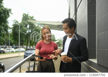 Two businesspeople discussing something important while walking along a modern building Two businesspeople discussing something important while walking along a modern building 118007792