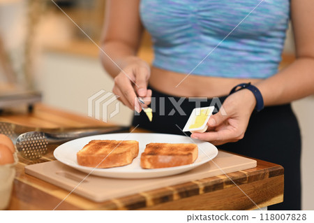 Close up image of young woman spreading butter on a piece of toast Close up image of young woman spreading butter on a piece of toast 118007828