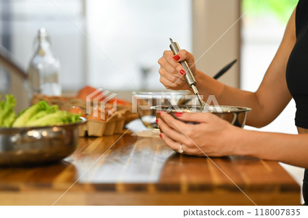 Cropped shot of woman preparing food on a wooden table, mixing ingredients in a metal bowl 118007835