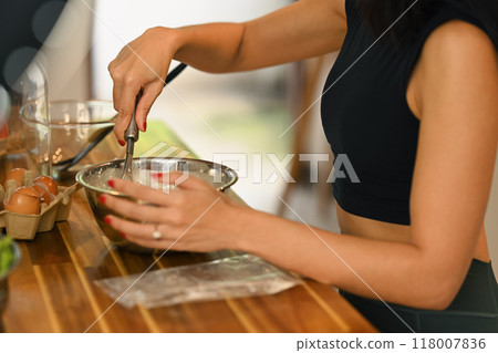 Cropped shot of woman preparing food on a wooden table, mixing ingredients in a metal bowl Cropped shot of woman preparing food on a wooden table, mixing ingredients in a metal bowl 118007836