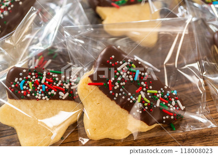 Carefully packaging Christmas cutout cookies, half-dipped in chocolate and presented in clear cellophane wrapping, perfect for festive gifting. Carefully packaging Christmas cutout cookies, half-dipped in chocolate and presented in clear cellophane wrapping, perfect for festive gifting. 118008023