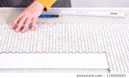 In the process of mounting peel and stick mosaic tiles onto a foam board, perfect for enhancing a food photography studio's aesthetic. 118008083