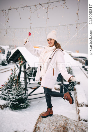 Enjoying winter magic with a lollipop while posing in a snowy landscape decorated with lights 118008817