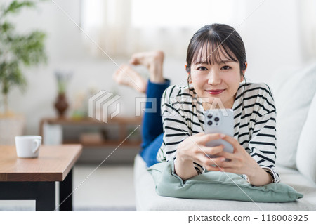 一名年輕女子在沙發上操作智慧型手機。 一名年輕女子在沙發上操作智慧型手機。 118008925