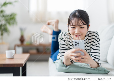 一名年輕女子在沙發上操作智慧型手機。 一名年輕女子在沙發上操作智慧型手機。 118008926