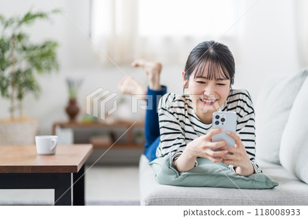 一名年輕女子在沙發上操作智慧型手機。 118008933