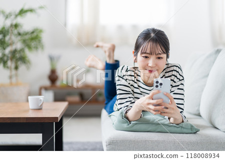 一名年輕女子在沙發上操作智慧型手機。 118008934