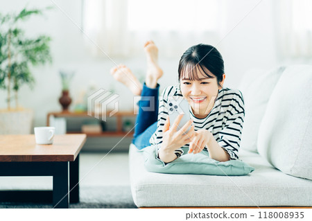 一名年輕女子在沙發上操作智慧型手機。 118008935