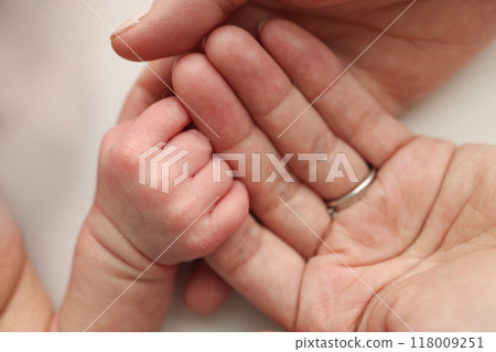 The newborn baby has a firm grip on the parent's finger after birth. Close-up little hand of child and palm of mother and father. Parenting, childcare and healthcare concept. The newborn baby has a firm grip on the parent's finger after birth. Close-up little hand of child and palm of mother and father. Parenting, childcare and healthcare concept. 118009251