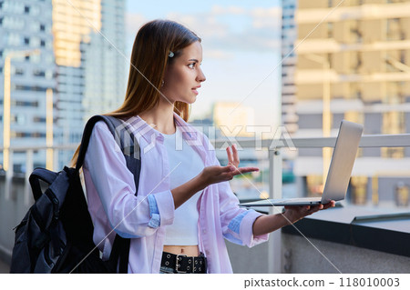 Teen female student using laptop for video chat, modern city background Teen female student using laptop for video chat, modern city background 118010003