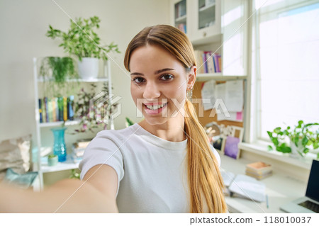 Close-up selfie portrait of teenage cheerful female looking at web camera Close-up selfie portrait of teenage cheerful female looking at web camera 118010037
