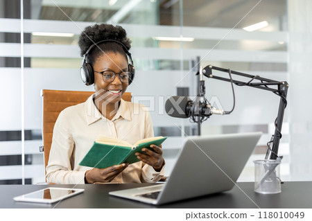 African American businesswoman using laptop and microphone for podcast recording. Concept of technology, broadcasting, and media. Professional and engaging work environment. 118010049