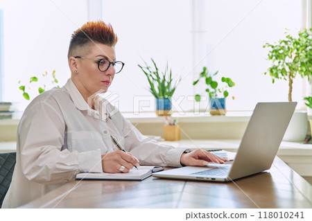 Middle-aged serious woman working at computer laptop in home office Middle-aged serious woman working at computer laptop in home office 118010241