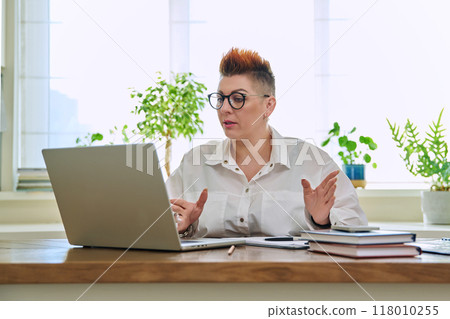 Middle aged businesswoman having video conference on laptop sitting at desk 118010255
